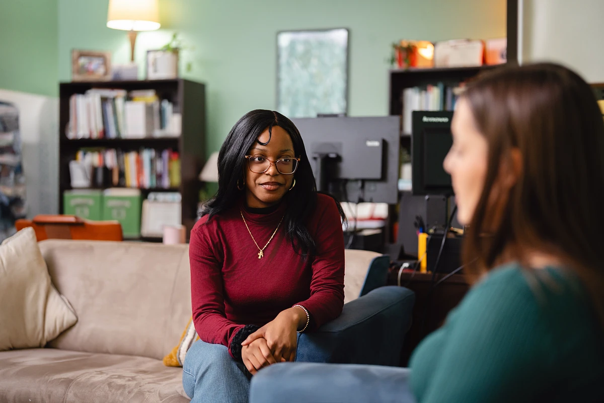 Two people are sitting across from each other in a cozy room, engaged in conversation.