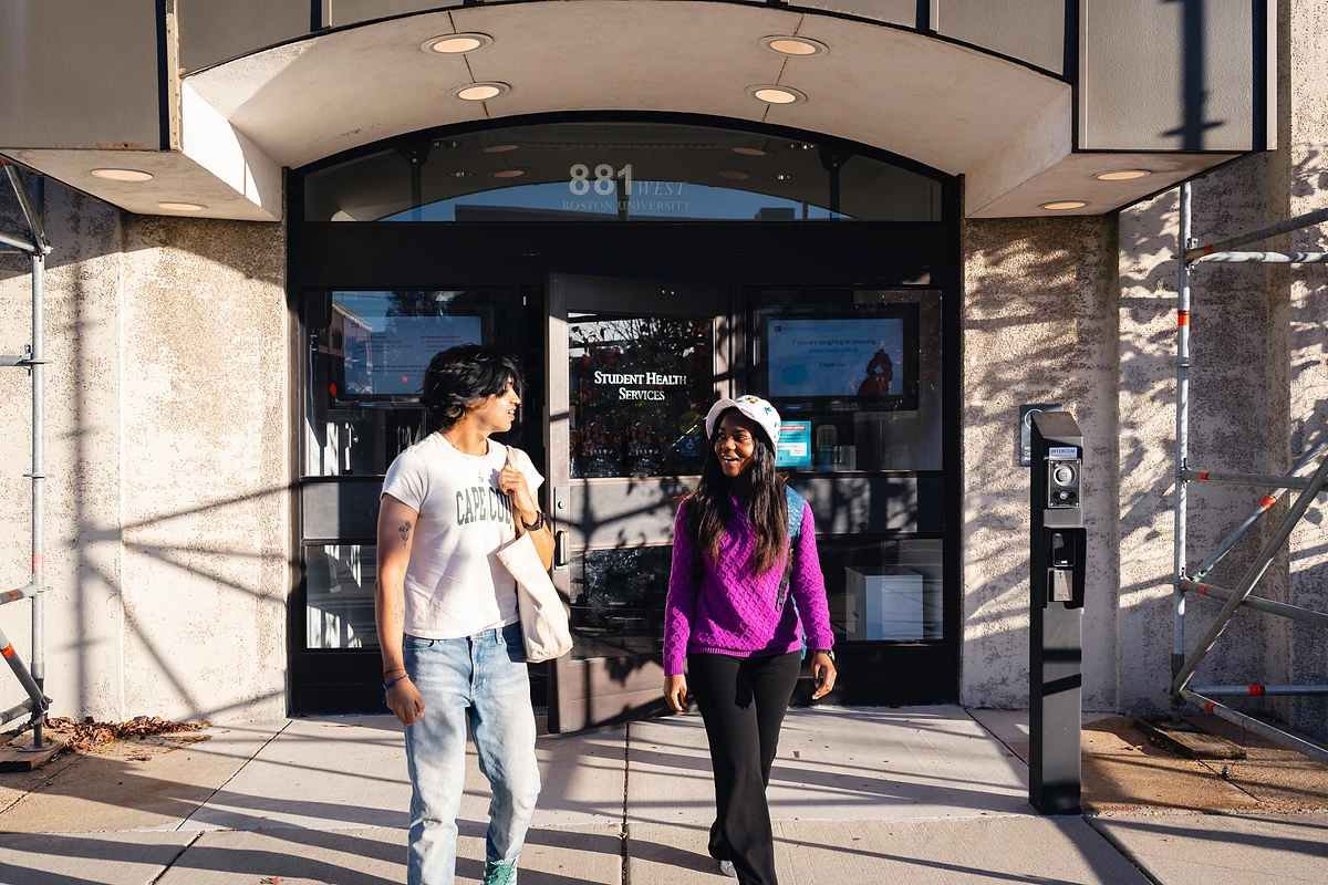 Two people are walking out of the Student Health Services building at Boston University.