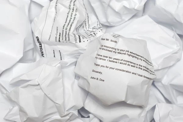The image shows crumpled resumes and cover letters scattered in a pile.